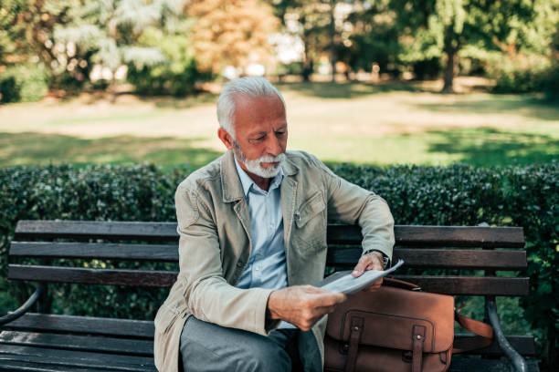 istock Senior man sitting on a bench and reading a book. 1067351568