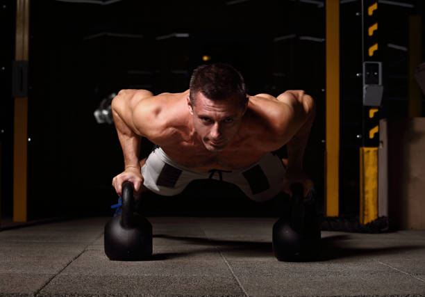 istock Handsome strong man doing plank on kettlebells, push-up on weights on dark sport club background. Training day 1067358152