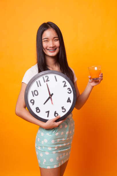 istock Asian woman with a clock drink orange juice. 1067361706
