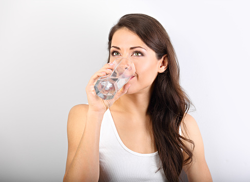 Positive happy smiling woman with healthy skin and long curly hair drinking pure water and looking up on white background.