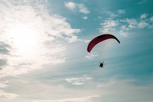 Motor paraglider flying in blue sky with white cloud in background.