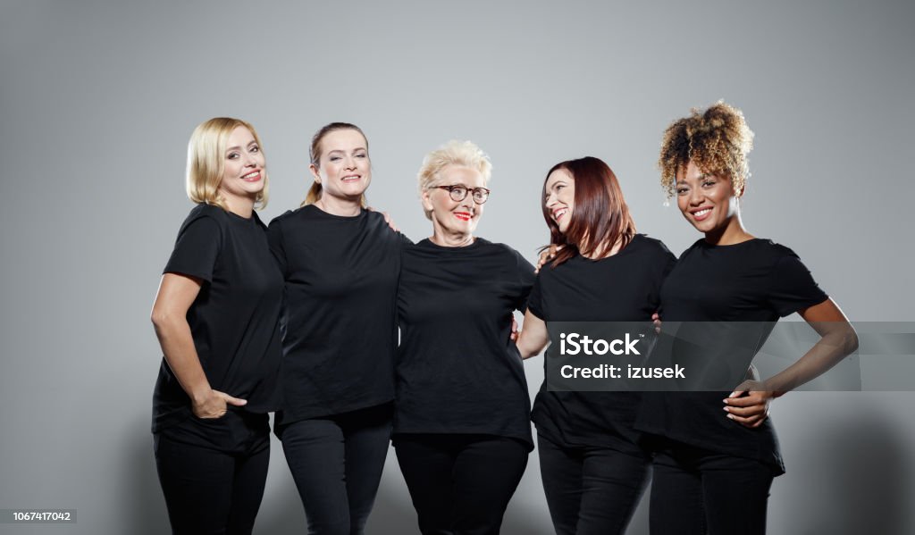 Group of powerful women Portrait of pleased women wearing black clothes, embracing against grey background and smiling at camera. Studio shot. Women Stock Photo