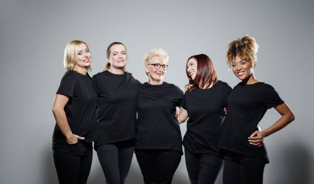 Group of powerful women Portrait of pleased women wearing black clothes, embracing against grey background and smiling at camera. Studio shot. unconventional wisdom stock pictures, royalty-free photos & images