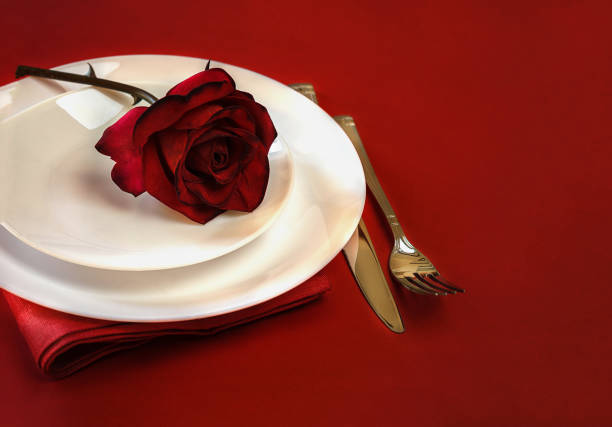 istock Romantic table setting for Valentines day or dinner date celebration wedding. Valentines day table setting with red rose bud, white plates, fork and knife on red tablecloth background. space for text 1067417270