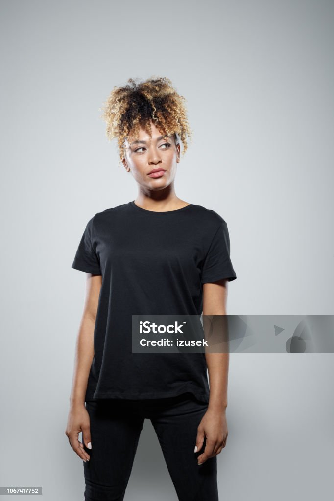 Portrait of confident young woman Strong young woman wearing black clothes, standing against grey background, looking away. Studio shot. Afro Hairstyle Stock Photo