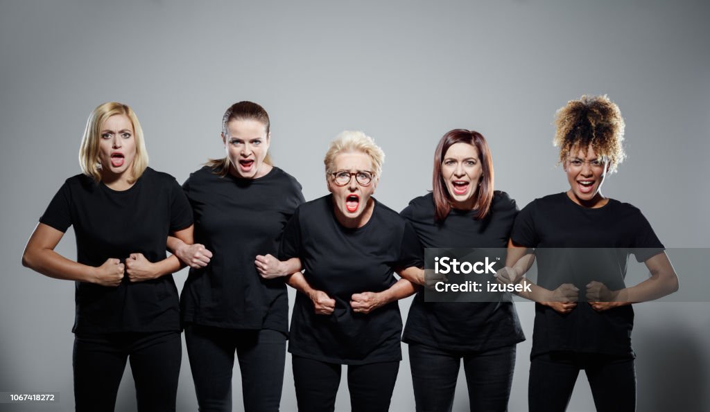 Group of angry women protesting Group of displeased women wearing black clothes, holding hands and screaming at the camera. Studio shot against grey background. Protest Stock Photo