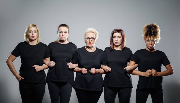Empowered women Group of displeased women wearing black clothes, holding hands and screaming at the camera. Studio shot against grey background. arm in arm stock pictures, royalty-free photos & images