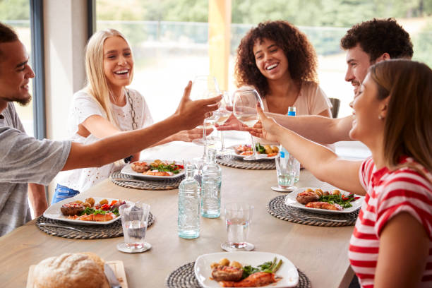 grupo étnico multi de cinco felizes jovens adultos amigos rindo e levantando os óculos de brinde durante um jantar - couple dinner summer sunlight - fotografias e filmes do acervo