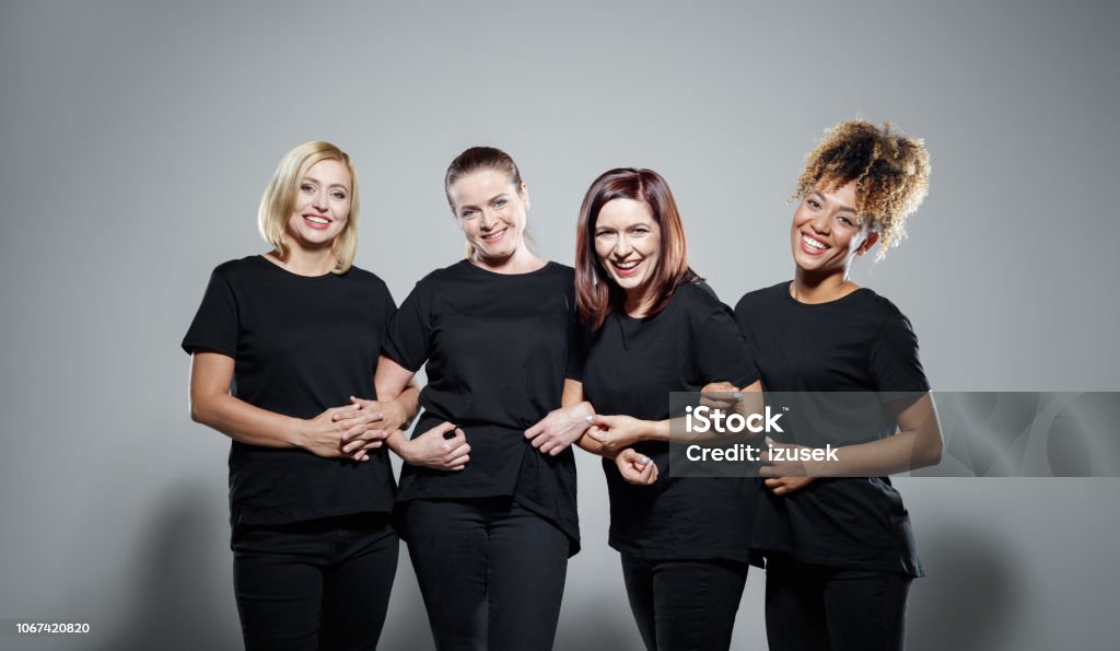 Group of powerful women Portrait of pleased women wearing black clothes, embracing against grey background and smiling at camera. Studio shot. Women Stock Photo