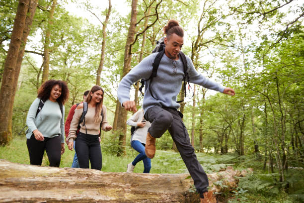 multi-ethnische gruppe von fünf jungen erwachsenen freunden im wald laufen und springen über umgestürzten baum während einer wanderung - couple young adult african descent multi ethnic group stock-fotos und bilder