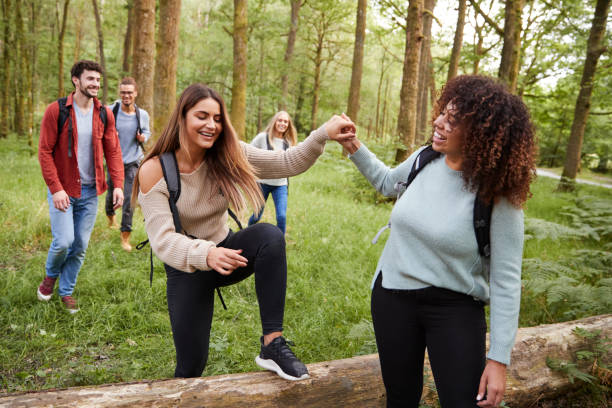 istock Young woman helping girlfriend step over a fallen tree during a hike with friends in a forest 1067421640