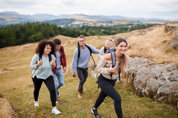 Multi ethnic group of five young adult friends hiking across a field uphill towards the summit, close up Multi ethnic group of five young adult friends hiking across a field uphill towards the summit, close up couple adventure activity adult stock pictures, royalty-free photos & images