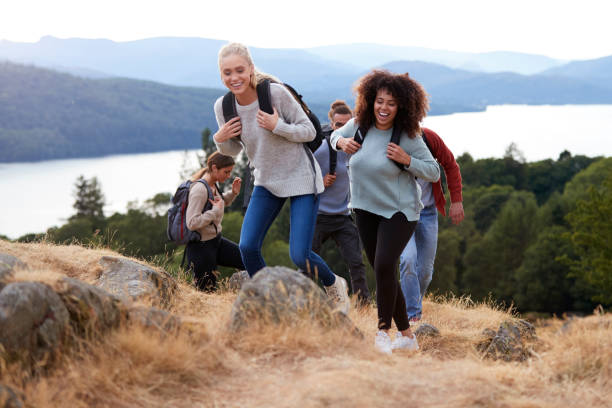 um grupo de cinco jovens amigos adultos sorrindo enquanto caminhadas juntos até um cume de montanha - adventure african ethnicity rural scene day - fotografias e filmes do acervo