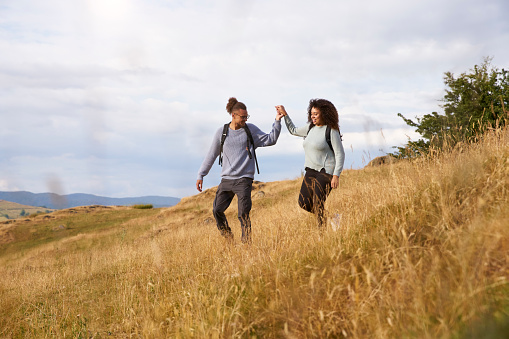 Young adult mixed race couple walking down a hill hand in hand during a mountain hike