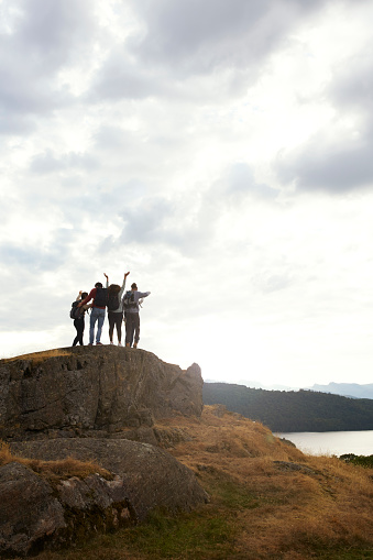 A silhouetted group of young adult friends celebrate arriving at the summit after a mountain hike