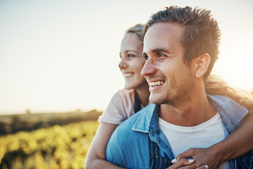 Cropped shot of a handsome young man piggybacking his girlfriend through the crops on their farm