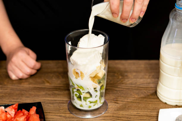 istock Cooking smoothies. Wooden table. Add cream to fruit. 1067429834