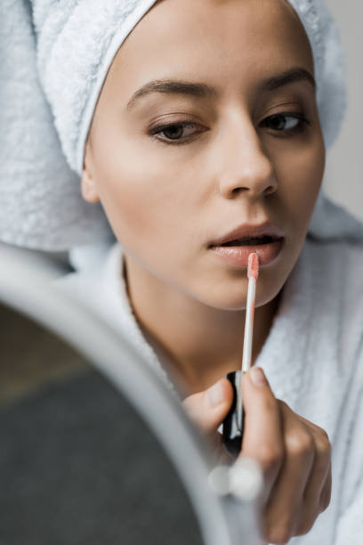 istock attractive young woman applying lip gloss and looking at mirror 1067431424
