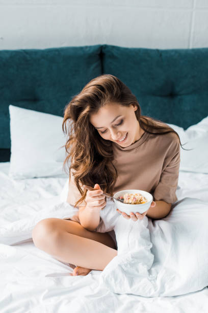 istock happy girl eating oatmeal for breakfast while sitting on bed 1067431626
