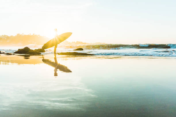 A surfer walking on the Zurriola Beach at sunset with the Monte Urgull in the background. San Sebastian, Basque Country, Guipuzcoa. Spain.