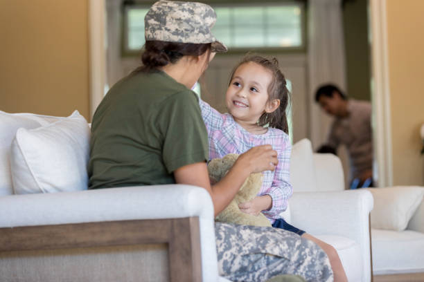 Little girl talks with military mom Smiling adorable little girl talks with her military mom after her mom's return from service. They are sitting on a sofa in their living room. proud army mom stock pictures, royalty-free photos & images