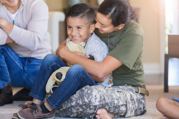 Military mom embraces cheerful son Cute little boy smiles as his military mom gives him a big hug from behind. They are sitting on the floor in their living room. proud army mom stock pictures, royalty-free photos & images
