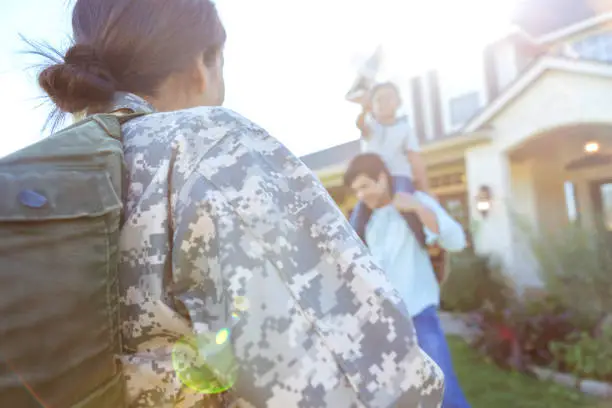 Rear view of mid adult female soldier returning home from military duty. Her husband and son are playing in the front yard.
