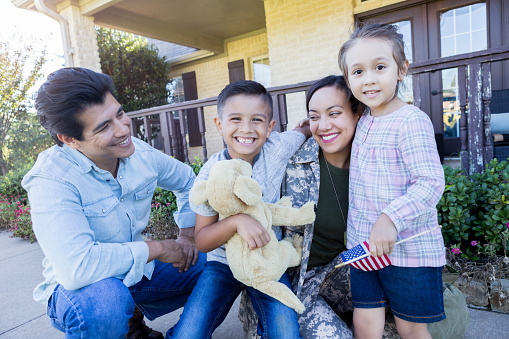 Excited mid adult female soldier is happy to be home from deployment. She is with her husband and two children in their front yard.
