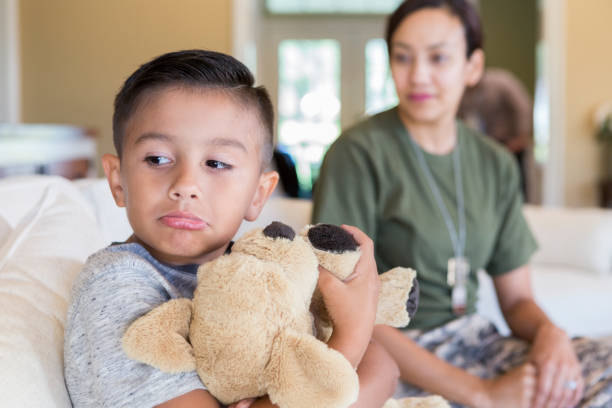 Sad little boy as mom prepares to leave for military service Elementary age boy pouts and ignores his mom because she is about to leave for overseas military assignment. The boy is hugging his stuffed animal. His mom is blurred in the background. proud army mom stock pictures, royalty-free photos & images