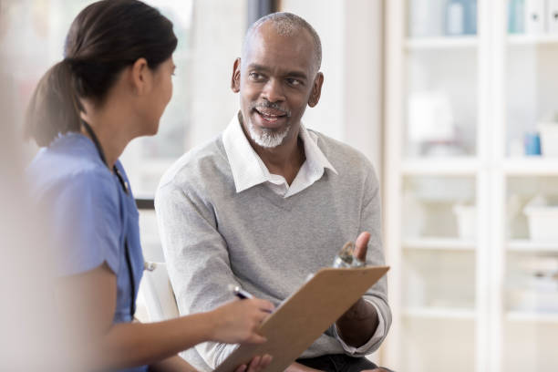 Senior man discusses diagnosis with doctor A cheerful senior man sits next to an unrecognizable female doctor in her office.  She holds a clipboard as he asks questions regarding his diagnosis. form filling photos stock pictures, royalty-free photos & images