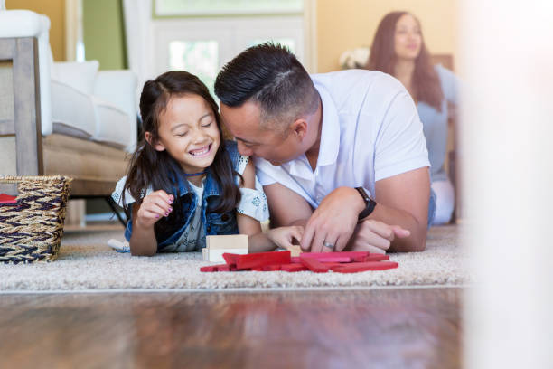 Cheerful dad and his cute little girl play with building blocks in their living room.