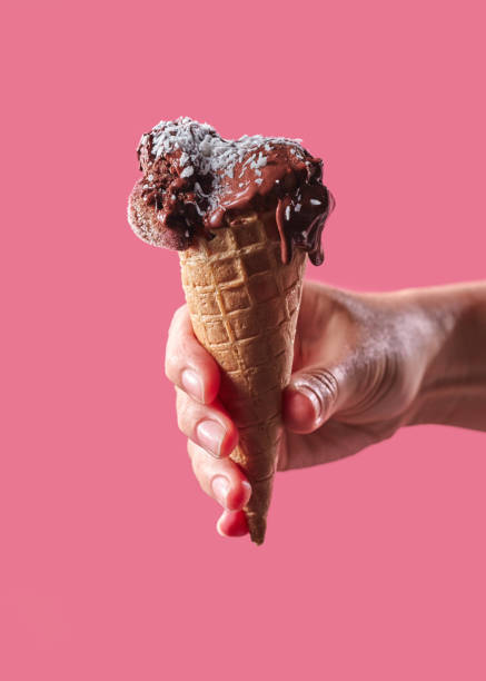 istock The hand of a man holds a waffle cone with fruit, ice cream decorated with coconut chips on a pink background with copy space. 1067458420