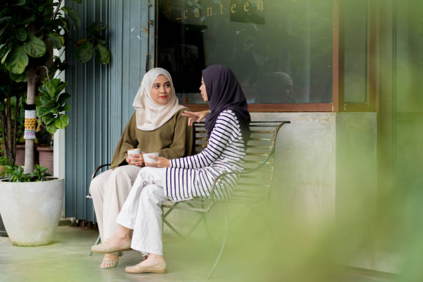 Friends sitting outside a cafe talking wearing a hijabs. Kuala Lumpur, Malaysia. April 2018