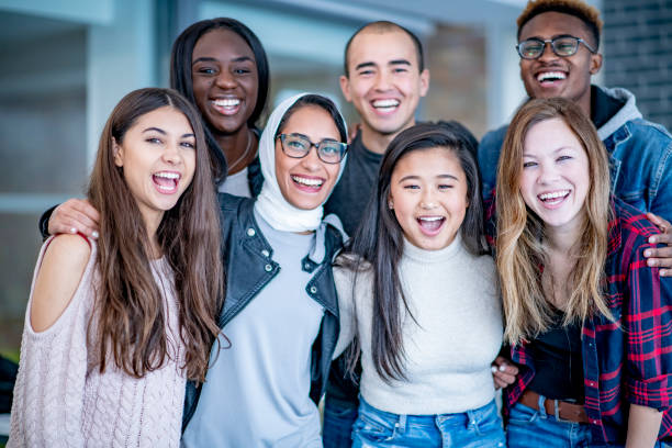 Portrait of a group of students with bright smiles A varying group of young adults stand and smile with their arms around each other. They could be university or college students. trainee stock pictures, royalty-free photos & images