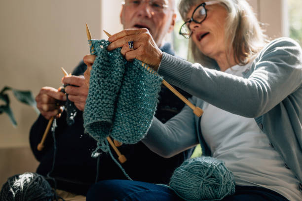 Senior couple knitting wool at home Senior woman teaching her husband the art of knitting woollen clothes. Senior man learning to knit woollen clothes from his wife sitting at home. knitting photos stock pictures, royalty-free photos & images