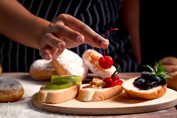 Photo of Close up Dessert Chef putting a cherry on a dessert recipe in a commercial kitchen. Sweet and Foods Idea Concept.