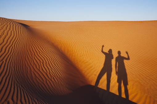 Shadows of two friends waving on greeting. Sand dunes in Oman desert.