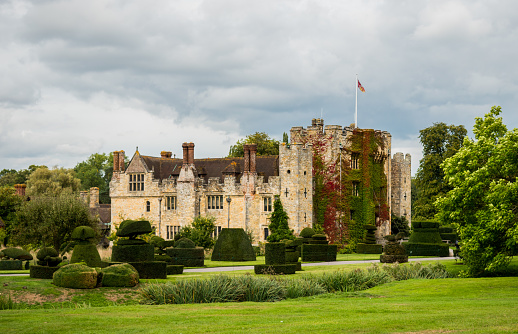 Hever Castle, England, UK – September 08 2018: View of Hever Castle and its topiary garden on a cloudy day, with a flag flying at full mast. Hever Castle was the childhood home of Anne Boleyn.