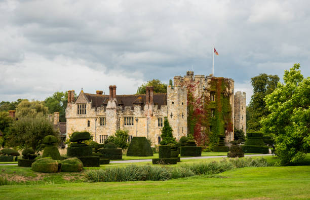 View of Hever Castle and its topiary garden on a cloudy day Hever Castle, England, UK – September 08 2018: View of Hever Castle and its topiary garden on a cloudy day, with a flag flying at full mast. Hever Castle was the childhood home of Anne Boleyn. Hever Castle stock pictures, royalty-free photos & images