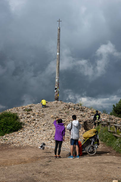 Cruz de Ferro on Camino de Santiago near Foncebadon, Spain A man and woman from Taiwan, their two young children in the modified stroller, stand at the Cruz de Ferro, or Iron Cross, a landmark on the Camino de Santiago. Here many pilgrims deposit a stone brought from home. (July 2018) iron cross stock pictures, royalty-free photos & images