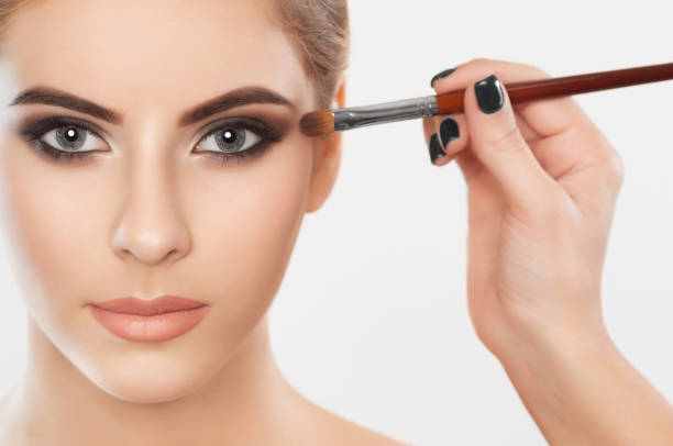 le maquilleur peint des sourcils et des yeux d’une belle jeune fille. - make up makeup artist make up brush applying photos et images de collection