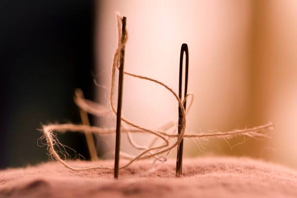 Needles. Close up of two needles sticking in a dusky pink pincushion. Macro shot. Side view. One needle with visible needle eye. Threads curved around. Individual fibers visible. Blurred dusky pink background. needles eye stock pictures, royalty-free photos & images