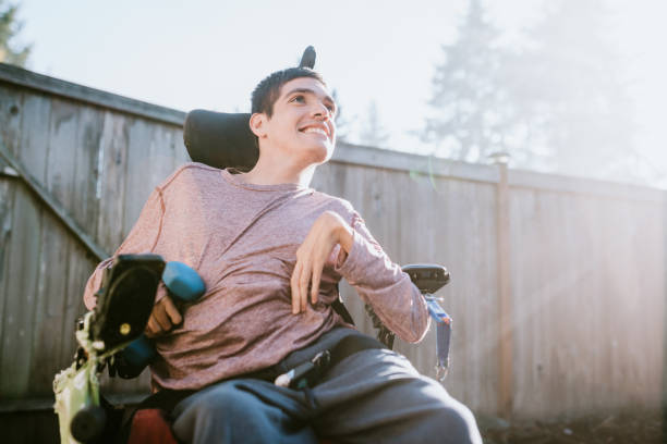 Confident Young Man In Wheelchair At Home A cheerful young adult man with cerebral palsy smiles outdoors, holding a small dumbbell weight. developmental disability stock pictures, royalty-free photos & images