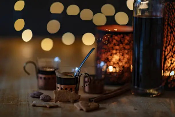 Mulled wine in small glasses on a table. Candles are lit behind them and blurry fairy lights can be seen in the background.