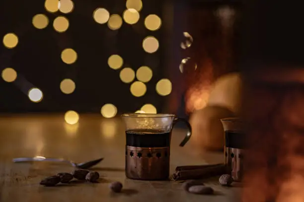 Mulled wine in small glasses on a table. Nuts are laying next to them and blurry fairy lights can be seen in the background.