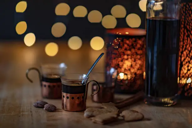 Mulled wine in small glasses on a table. Candles are lit behind them and blurry fairy lights can be seen in the background.
