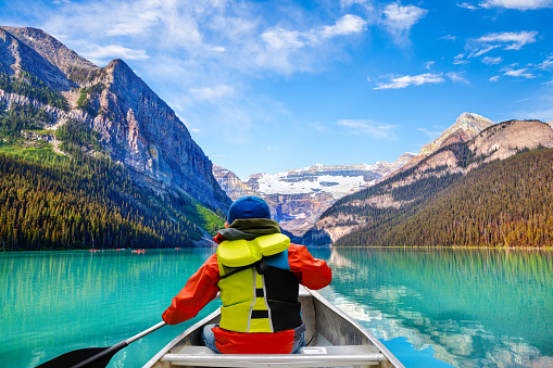 Teen boy canoeing on Lake Louise in Banff National Park of the Canadian Rockies with its glacier-fed turquoise lakes and Mount Victoria Glacier in the background.