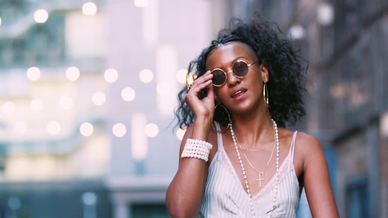 Young black woman dancing and singing on the street, low angle, bokeh lights in background