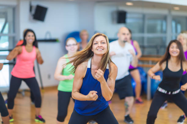 Dance fitness A woman in a dance workout class smiles at the camera. They are all in sportswear and moving to the side. fitness boot camp stock pictures, royalty-free photos & images