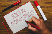 Word writing text Seo and Adwords. Business concept for Pay per click Digital marketing Google Adsense Man hand holding marker notebook paper expressing ideas wooden background.
